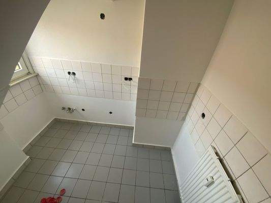 Kleine Küche mit grauen Bodenfliesen, weißen Fliesespiegel, weißen Wänden, Dachschräge und Fenster.jpg