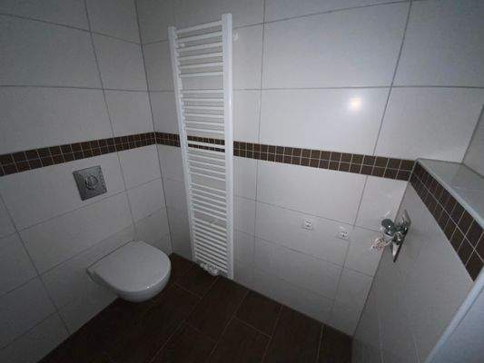 Blick in Bad mit weißen Wandfliesen, braunen Bodenfliesen Hänge-WC und ebenerdiger Dusche 