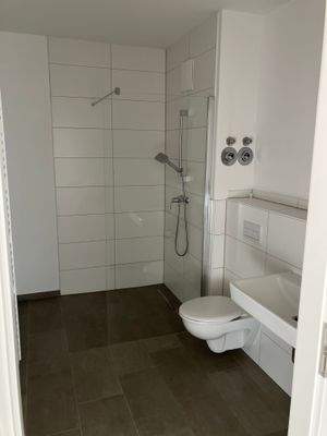 Bad mit bodengleicher Dusche, weißen Sanitärobjekten, weißen Wandfliesen und dunkelgrauen Bodenfliesen