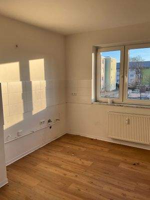 Küche mit braunem Vinylboden. Decke und Wände weiß angelegt. Weißer Fliesenspiegel mit Steckdose. Großes Fenster