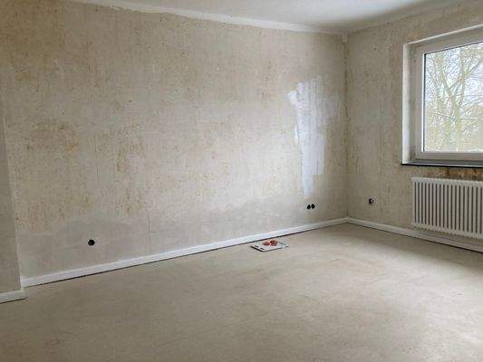 Wohnzimmer mit weißem Fenster, weißem Heizkörper und tapetenlosen Wänden.