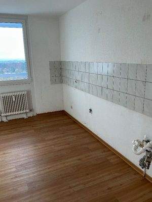 Küche mit weißen Wänden, weiß/grauem Fliesenspiegel, sowie Design-Vinylboden in Holzoptik.