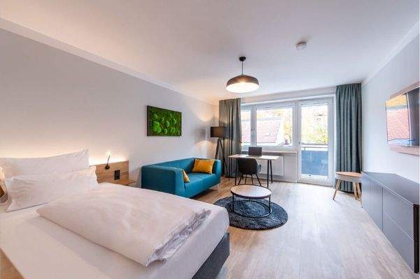 Schlafzimmer 1 mit Balkon, Bett, Couch, TV und Arbeitsbereich