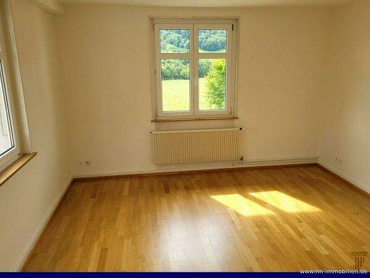 Helles Zimmer mit Parkettboden und grossem Fenster mit Blick ins Grüne