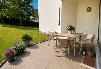 Die Gartenterrasse mit Sondernutzungsrecht an einem Wiesenanteil. Gesetzlich vorgeschriebener Hinweis: Dies Foto wurde mit KI bearbeitet, also KI generiert - hier speziell nur die Möblierung und die Pflanzenkübel.