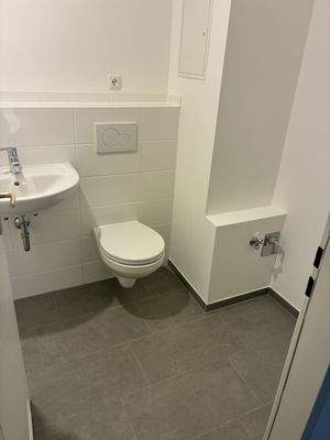 Badezimmer mit Badewanne. Ohne Fenster. Decke und Wände weiß gestrichen. Neu weiße Wandfliesen und dunkle Bodenfliesen. Mit Waschmaschinenanschluss