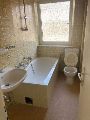 Tageslichtbad mit Badewanne, weißen Sanitärobjekten, gelben Wandfliesen und hellbraunem Linoleumboden