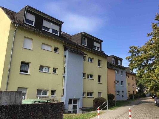 Eingangsbereich des mehrstöckigen Wohngebäudes umgeben von Grünanlagen mit Bäumen und Sträuchern