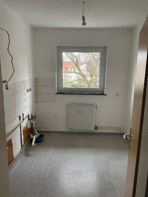 Küche mit Fenster und weißem Fliesenspiegel. Die Wände sind weiß gestrichen und es ist ein grauer PVC Boden verlegt.