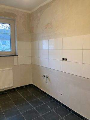 Küche mit dunkelgrauen Bodenfliesen und einem weißem Fliesenspiegel.