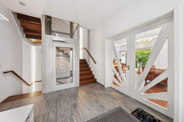 Großzügiges Entrée mit gläsernem St.Gobain Lift und maßgefertigter Flügeltür aus lackierter Buche mit Glaseinsätzen