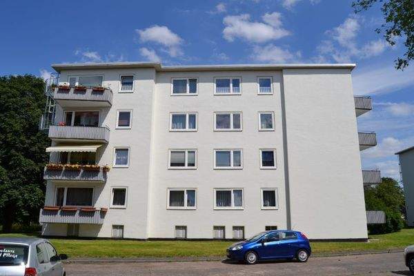  Seitenansicht eines mehrstöckigen  Wohngebäudes mit Balkonen, umgeben von Bäumen und grünen  Sträuchern 