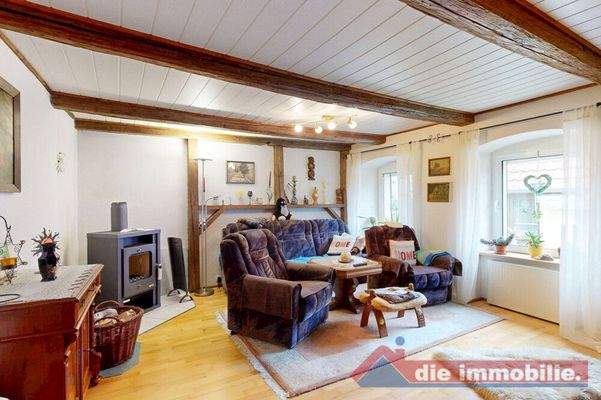 Wohnzimmer mit sichtbaren Holzbalken und Kaminofen – der gemütliche Mittelpunkt des Hauses