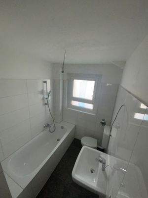 Modernisiertes Badezimmer mit Tageslicht, weißer Badewanne, weißem Wandwaschbecken, weißem Stand-WC, weißen Wandfliesen und grauen Bodenfliesen