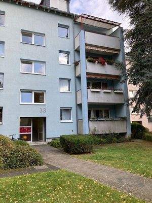 Eingangsbereich des mehrstöckigen Wohngebäudes umgeben von Grünanlagen mit Bäumen