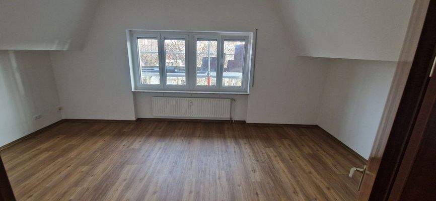 Vorderansicht eines mehrstöckigen Wohngebäudes mit Balkonen umgeben von Bäumen und grünen Sträuchern.