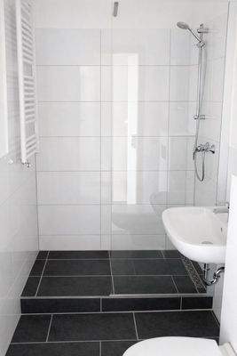 Badezimmer mit Dusche, weiß gefliest mit grauem Fliesenboden.jpg