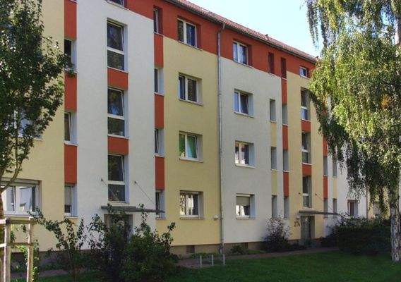 Vorderansicht eines mehrstöckigen Wohngebäudes umgeben von Bäumen und grünen Sträuchern.