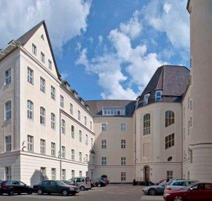 Heller Innenhof mit historischem Bürogebäude, mehreren geparkten Autos und Fensterfassade mit Walmdach.