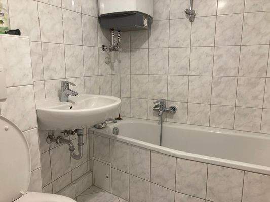 Badezimmer mit weiß-grau-melierten Fliesen, Badewanne, Handwaschbecken und Toilette.