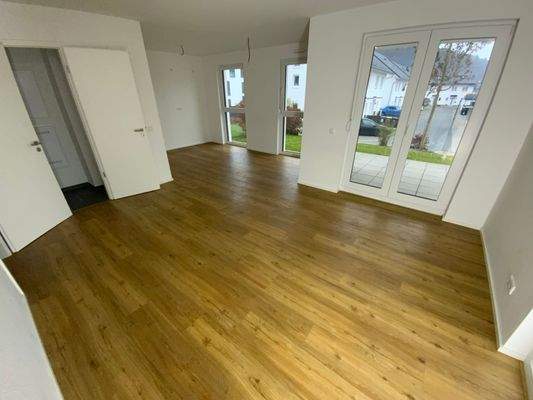 Wohnbereich mit offener Küche, Vinylboden in Holzoptik und weißen Wänden mit bodentiefen Fenstern 