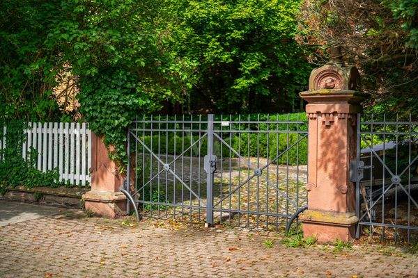 Schmiedeeisernes Eingangstor mit Sandsteinpfosten und begrünter Umgebung