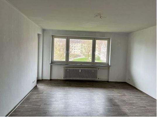 Wohn- und Essbereich mit Zugang zum Balkon, helle Wände und hellgrauer Bodenbelag in Holzoptik.JPG