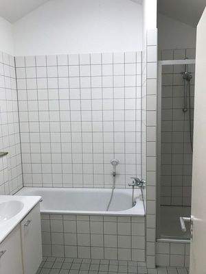 Weiß gefliestes Badezimmer mit weißen Sanitäreinrichtungen. Badewanne und Dusche