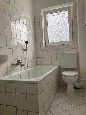 Tageslicht-Badezimmer mit weiß-marmorierten Fliesen, weißem Stand-WC und einer Badewanne.