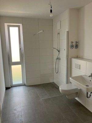 Tageslichtbad mit Dusche, weißen Sanitärobjekten, weißen Wandfliesen, dunkelgrauen Bodenfliesen und Waschmaschinenanschluss