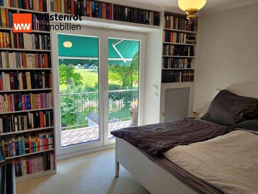 Schlafzimmer mit integrierten Wandregalen und Zugang zum Balkon mit Außenmarkise