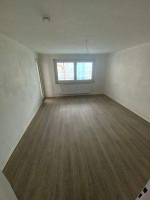 Wohnzimmer mit weiß grundierten Wänden, Fenster, Balkontür und Designerboden in Holzoptik