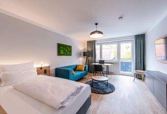 Schlafzimmer 1 mit Balkon, Bett, Couch, TV und Arbeitsbereich