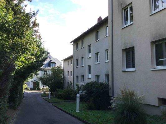 Vorderansicht eines mehrstöckigen Wohngebäudes umgeben von Bäumen und grünen Sträuchern.