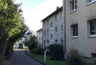 Vorderansicht eines mehrstöckigen Wohngebäudes umgeben von Bäumen und grünen Sträuchern.