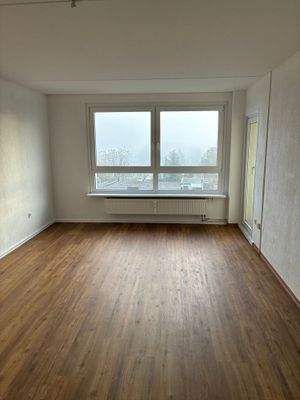 Wohnzimmer mit Zugang zum Balkon, weiß angelegte Wände, brauner Vinyl-Designboden