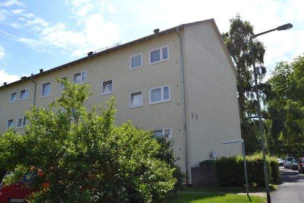 Seitenansicht eines mehrstöckigen  Wohngebäudes mit Balkonen, umgeben von Bäumen und grünen  Sträuchern 