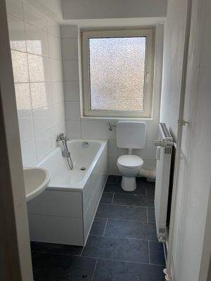 Bad mit Badewanne, weißen Sanitärobjekten, weißem Fliesenspiegel und dunkelgrauen Bodenfliesen