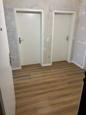 Blick in den Flur. Weiße Türen und neuer brauner Vinylboden. Decken weiß angelegt. Wände tapezierfähig.