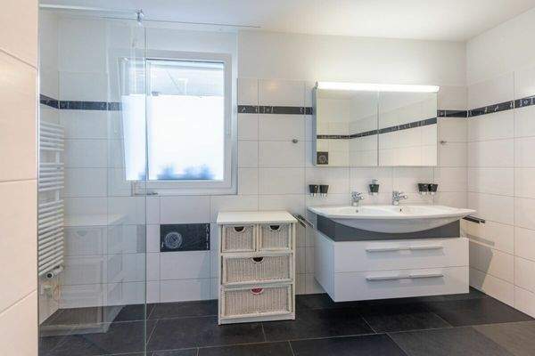 Badezimmer mit Fenster, bodenebener Dusche, grosser Badewanne und Doppel-Lavabo sowie WC