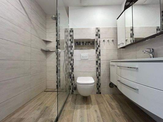 Die nahezu bodengleiche Dusche ist in die Ecke gebaut und kommt ohne Tür aus