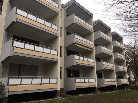 Frontansicht eines mehrstöckigen Gebäudes mit Balkonen, umgeben von Wiesen und Bäumen.