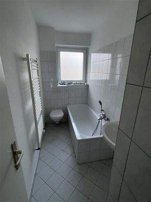 Badezimmer mit weißen Fliesen, Badewanne, Hänge-WC und Tageslicht-Fenster