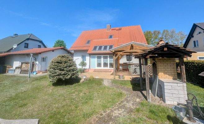 Blick vom Grundstück zum Wohnhaus (Gartensicht) mit überdachtem Grillofen im Vordergrund