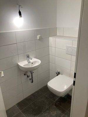 Weißgefliestes separates Gäste-WC mit dunkelgrauem Plattenboden