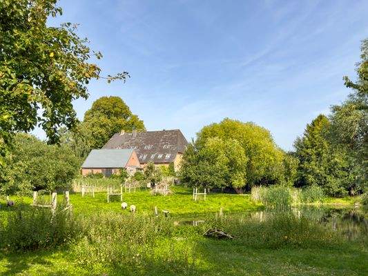 Blick aus dem Apfelgarten über den Teich in Richtung Haupthaus und Nebengebäude