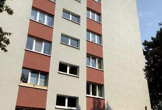 Außenansicht eines mehrstöckigen Wohnhauses, umgeben von Bäumen.  