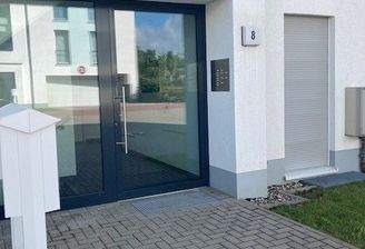 Blick auf den Hauseingang des weißen Hauses mit grauer Glaseingangstür