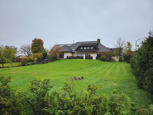 Der Blick auf das Haus mit Garten und grüner Einfriedung.png