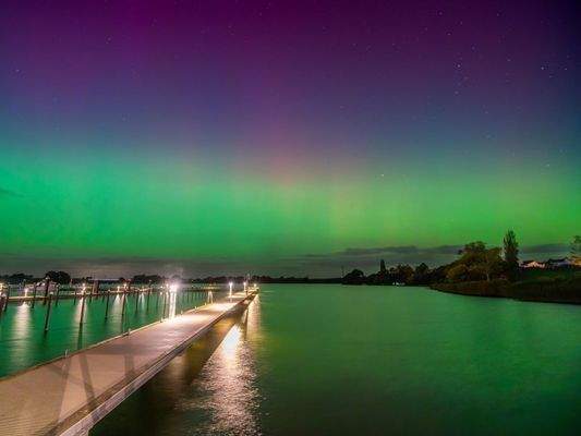 Polarlichter über den reetgedeckten Nachbarhäusern und dem Bootssteg in der Marina, Ansicht I